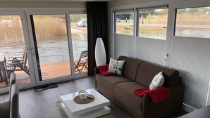 Una sala de estar moderna con un sofá marrón, una mesa de centro blanca y vistas a una masa de agua a través de amplios ventanales.