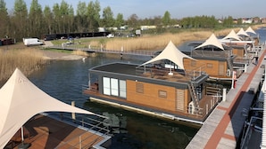 Alojamiento a orillas del río con terraza de madera, zona de estar cubierta y vistas al río y árboles.