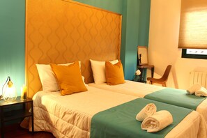 Une chambre d’hôtel avec deux lits, une table de chevet avec une lampe, une chaise et une fenêtre avec des stores.