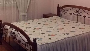 A bedroom with a wooden bed, a chandelier, a window with sheer curtains, and an air conditioning unit on the wall. - Family Apartment (Baku)