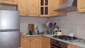 A kitchen with wooden cabinets, a stainless steel refrigerator, a gas stove, and a dish rack. - Family Apartment (Baku)