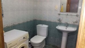 A small bathroom with a washing machine, toilet, and sink. - Family Apartment (Baku)
