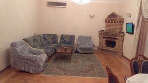 A living room with a sofa, armchair, small table, and a fireplace. - Family Apartment (Baku)