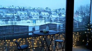 Enjoy a serene winter view from this cozy balcony with a table for two, a potted plant, and a bottle.