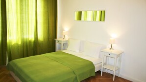 Una cama bien hecha con un edredón verde, dos mesitas de noche con lámparas y una cortina verde.