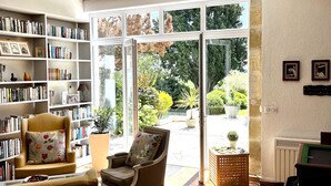 A spacious living room with a large bookshelf, two armchairs, a coffee table, and a view of the garden through a glass door. - "Paradise Found" Stunning Rural Setting - Pure Peace and Quiet 100% Guaranteed! (Ordan-Larroque)