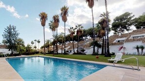 A swimming pool with a tiled deck, surrounded by palm trees and a white building with a tiled roof. - New Andalusian house (Marbella)