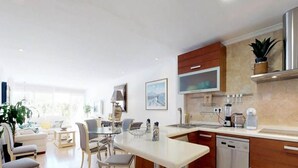 A modern kitchen with a dining area, featuring a central island, built-in appliances, and a large window providing natural light. - New Andalusian house (Marbella)