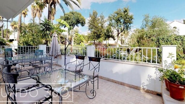 A glass-top table with chairs, a white railing, and potted plants on a balcony. - New Andalusian house (Marbella)