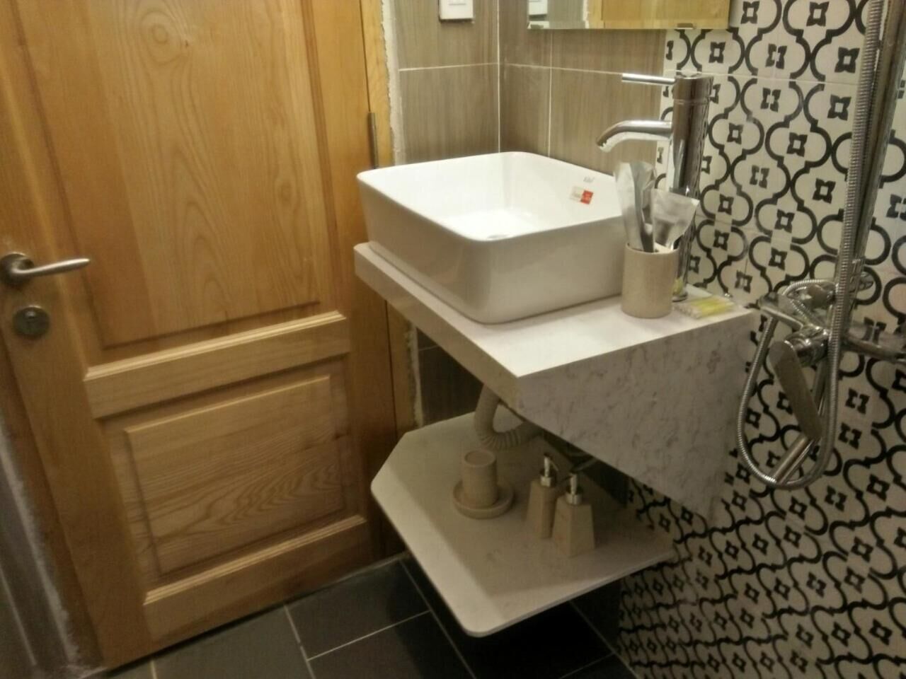 A bathroom with a wooden door, a white sink, a towel rack, and a patterned wall.
