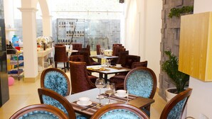 Un área de comedor con sillas de terciopelo, una mesa dispuesta con platos y vasos, y vista a la cocina al fondo.