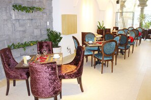 A dining area with a stone wall, a wooden table, and velvet chairs. - Emerald Ocean Hotel (Phu Thuy)