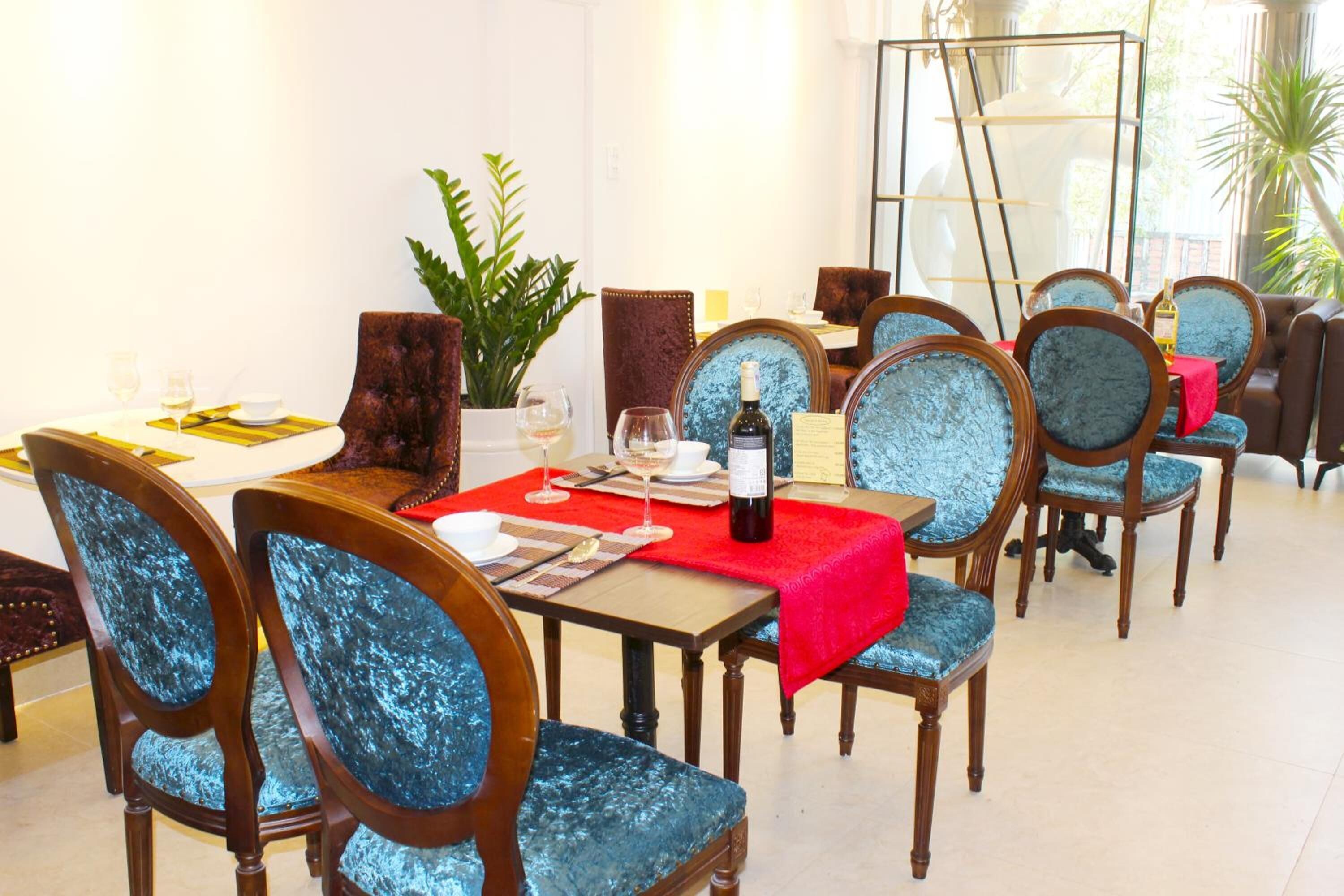 A dining area with wooden chairs and tables, a red tablecloth, and a bottle of wine on one table.