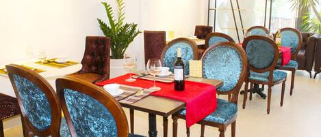 A dining area with wooden chairs and tables, a red tablecloth, and a bottle of wine on one table.