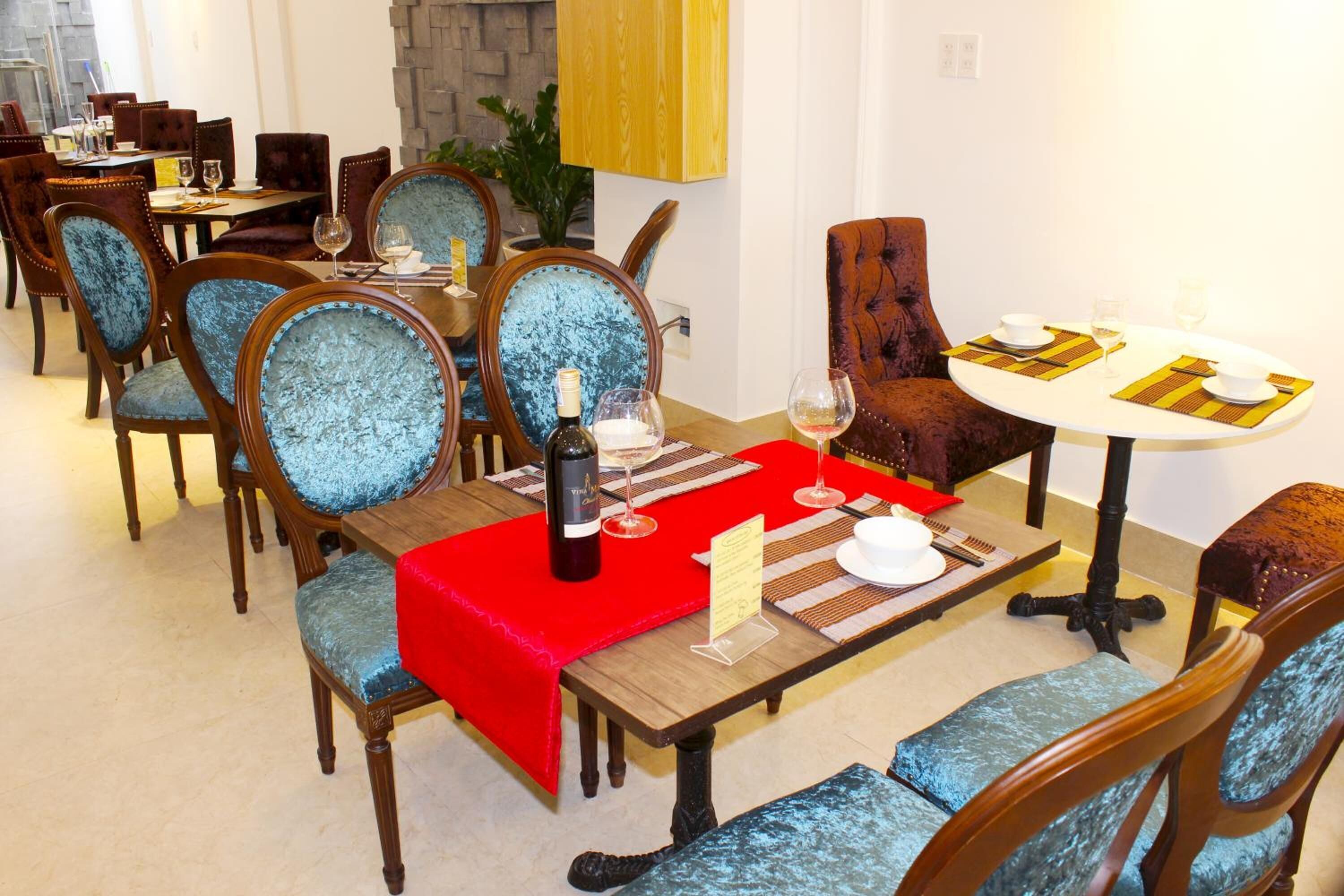 A dining area with wooden tables and chairs, red tablecloths, and a bottle of wine.