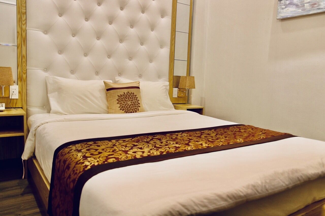 Una cama bien hecha con cabecera capitonada, ropa de cama blanca y un cojín decorativo.