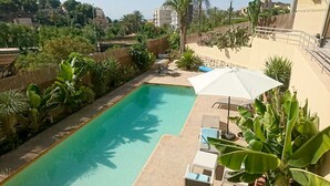 A swimming pool with lounge chairs and umbrellas, surrounded by greenery and a stone wall. - Guesthouse -El campello-Alacant (El Campello)
