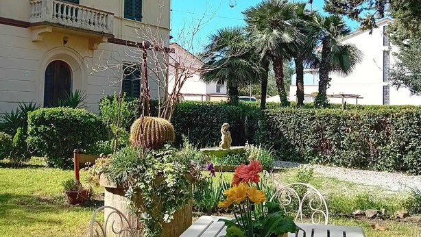 A courtyard with a white metal table, potted plants, and a building with a balcony. - Butterfly house. Apartment in Villa. Shared swimming pool and large park (Torre del Lago Puccini)