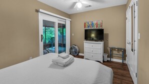 Ein Schlafzimmer mit einem großen Bett, einem Fernseher, einem Ventilator und einer Schiebetür zu einem Außenbereich.
