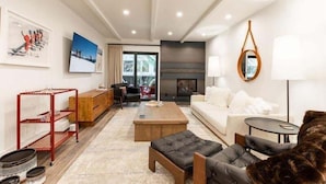 A modern living room with a sofa, coffee table, and a fireplace. There is a red metal shelf and a wooden cabinet. - Villa Cortina Condo with 5 Minutes Walk to Gondola by RedAwning (Vail)