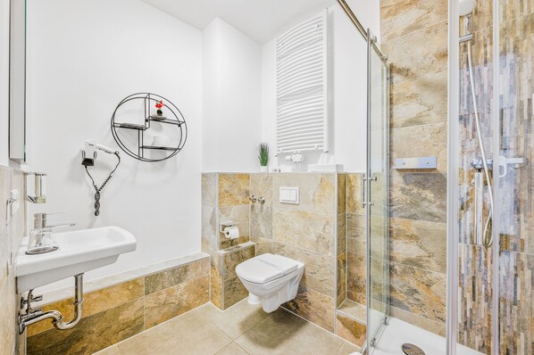 Un baño moderno con cabina de ducha de vidrio, un lavamanos blanco y un inodoro.
