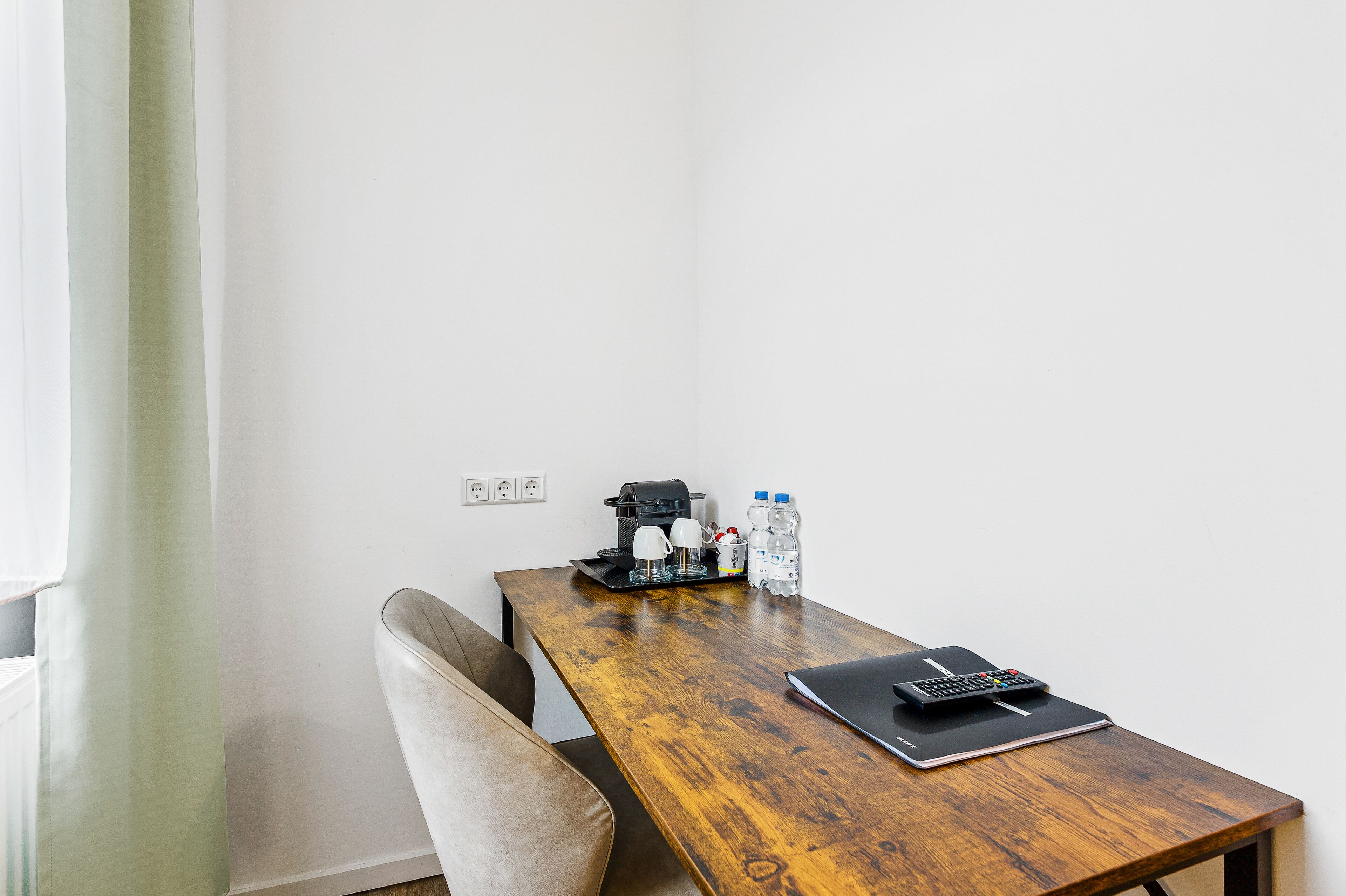 A small, wooden table with a laptop, a calculator, a coffee maker, and two water bottles.