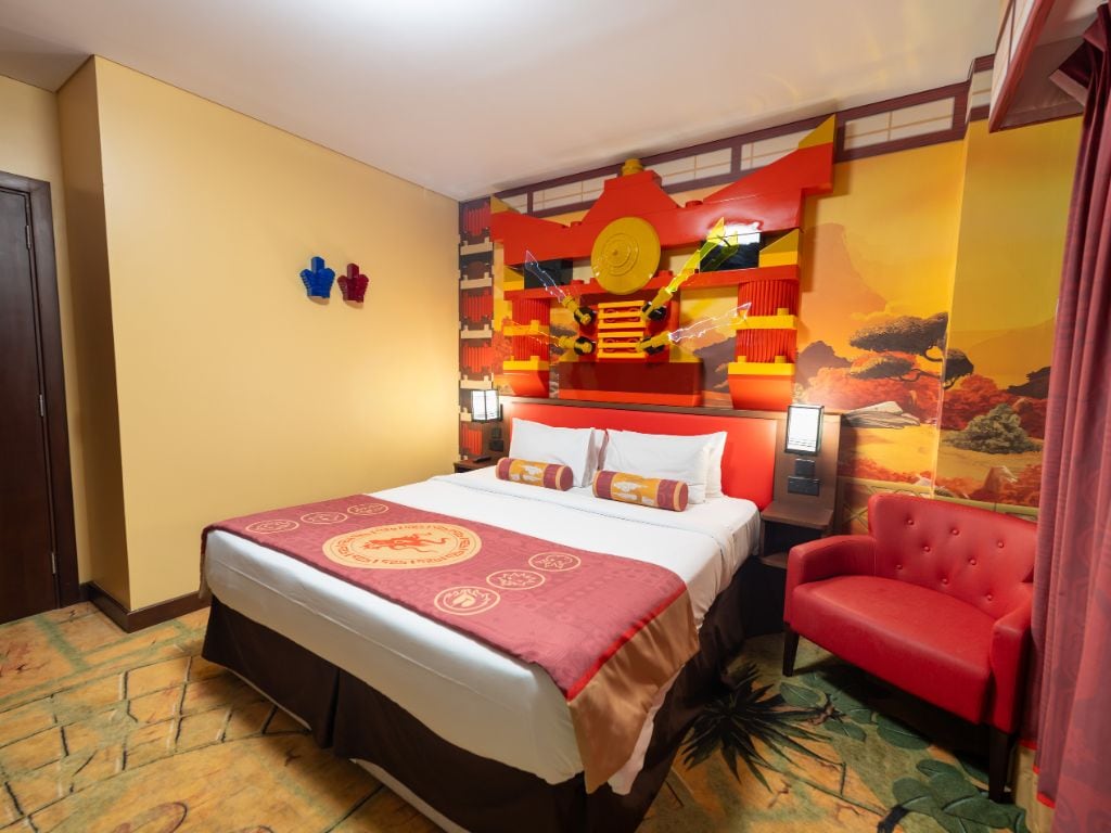 Une chambre d’hôtel avec un lit, un fauteuil rouge et une fresque murale.