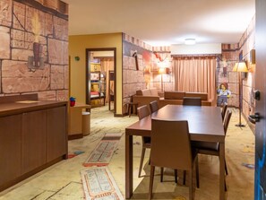 A dining area with a long table and chairs, a kitchen area with a counter, and a wall with a stone-like texture. - LEGOLAND Hotel Dubai (Dubai)