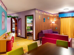 Una sala de juegos infantil con una zona de juegos de madera, un sofá morado y una mesa de comedor con sillas de colores.