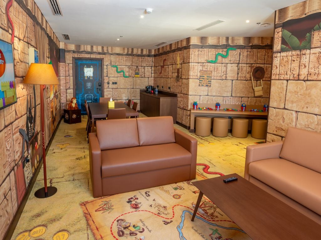 Ein Zimmer mit Wandgemälde aus Stein, einem braunen Sofa, einem kleinen Tisch und einer Lampe.