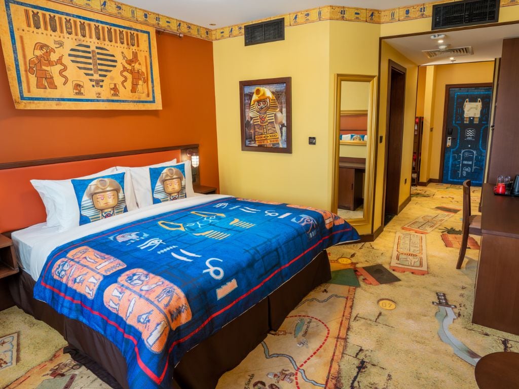 A hotel room with a bed, a large wall mural, and a door leading to another room.