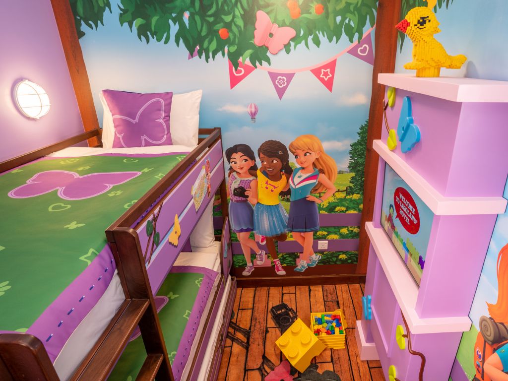 A children's playroom with a bunk bed, a mural, and a shelf with toys.