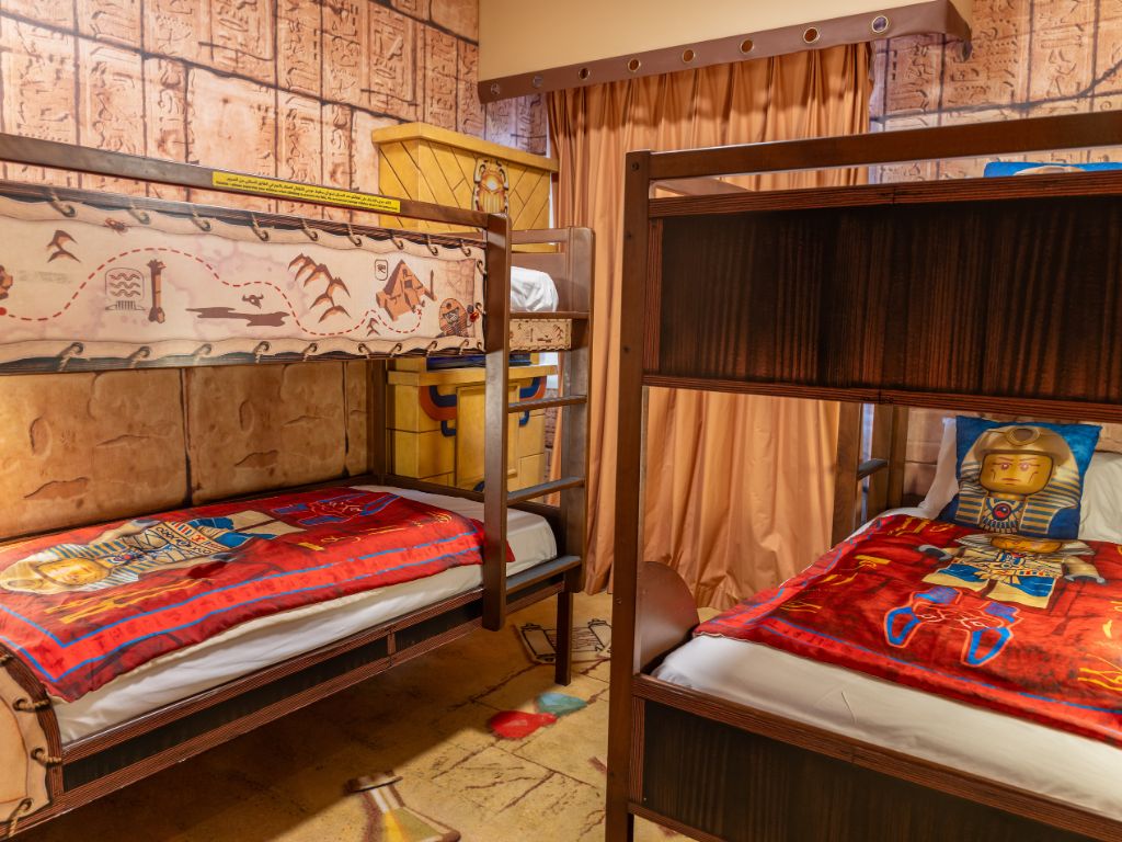 A room with two bunk beds, one with a map-themed bedspread and the other with a bedspread featuring a pyramid and an Egyptian figure.