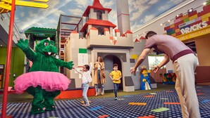 A play area with a castle structure, a green dinosaur mascot, and a LEGO Bricks restaurant in the background. - LEGOLAND Hotel Dubai (Dubai)