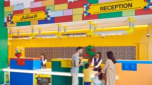Un espace d’accueil aux couleurs vives, agrémenté d’un décor sur le thème de LEGO, d’un comptoir d’accueil et d’un membre du personnel qui assiste les visiteurs.