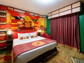 Habitación de hotel con una cama, una silla roja, una cortina y una pared con un diseño colorido.