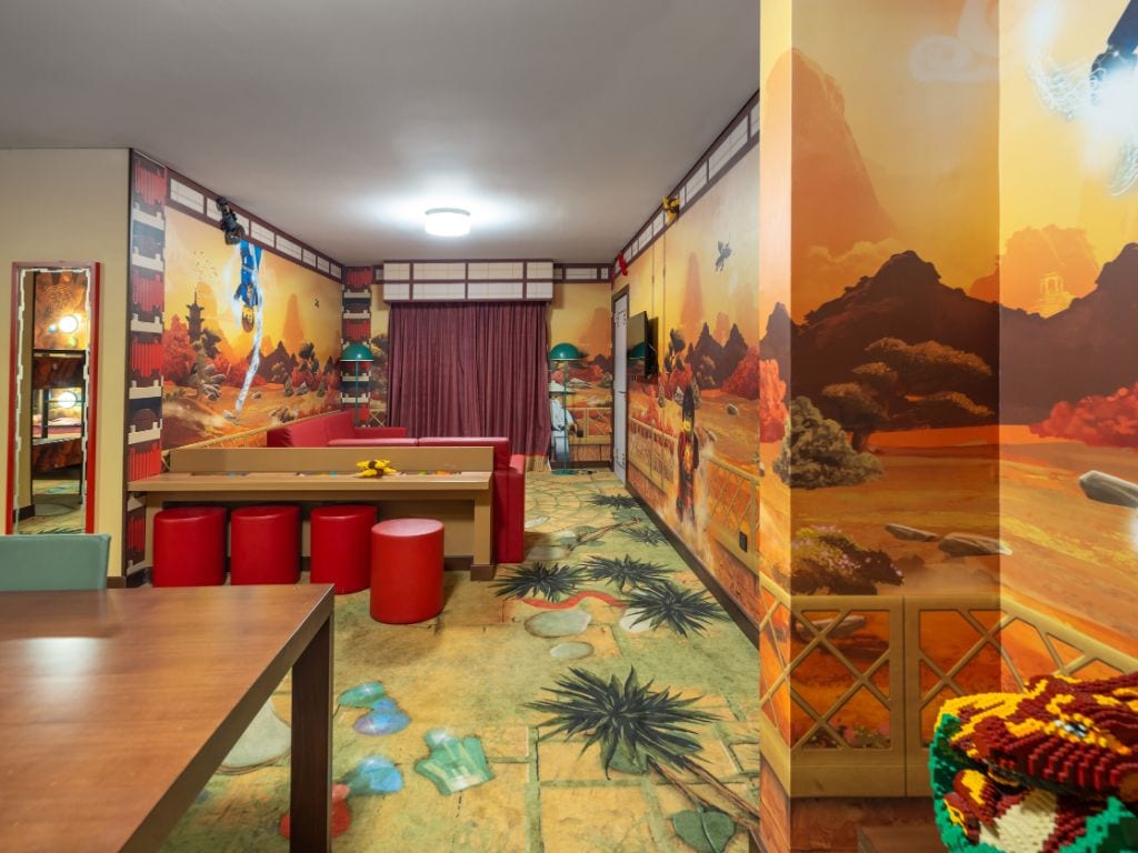 Quarto com mural, cama, escrivaninha e banquinhos vermelhos.