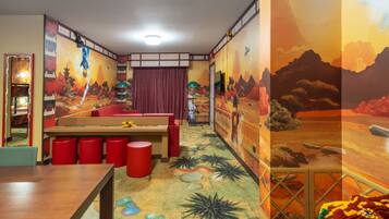 Quarto com mural, cama, escrivaninha e banquinhos vermelhos.