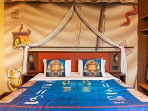 A bed with a canopy, two pillows with a pharaoh design, a blue bedspread with Egyptian symbols, and a nightstand with a lamp. - LEGOLAND Hotel Dubai (Dubai)