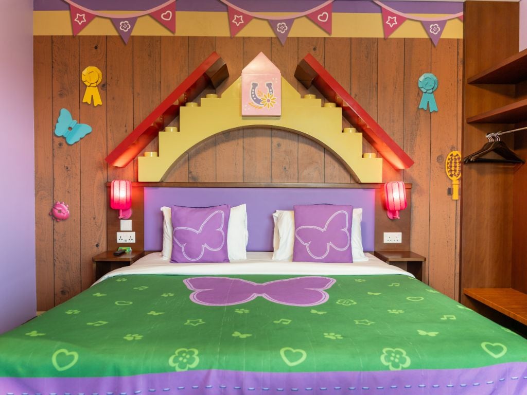 A room with a bed, wooden headboard, decorative pillows, and wall-mounted lights.