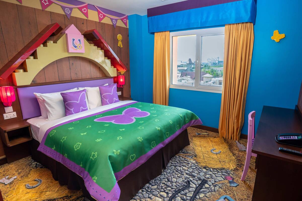 Habitación de hotel con cama, escritorio, ventana con cortinas y vista a la ciudad, además de un cartel en la pared.