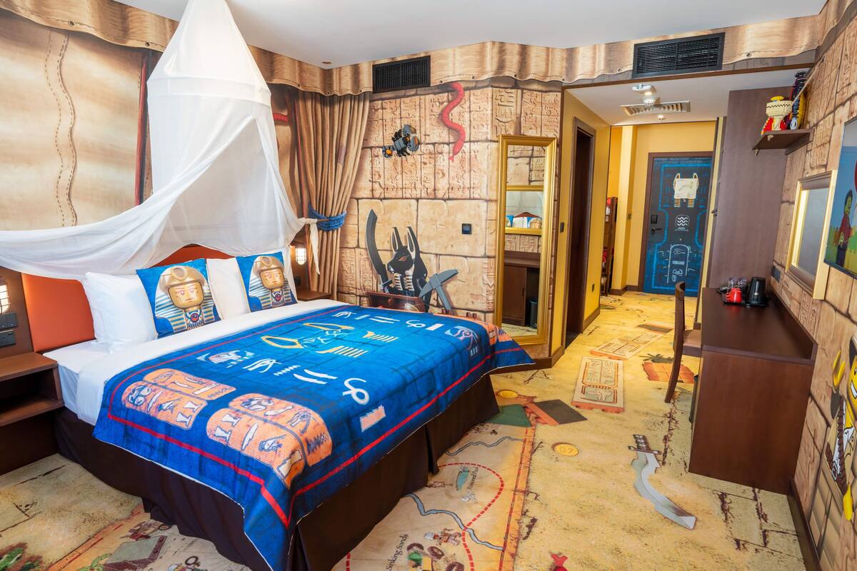 Una habitación de hotel temática con una cama, una mesita de noche, un armario y una puerta que da a otra habitación.