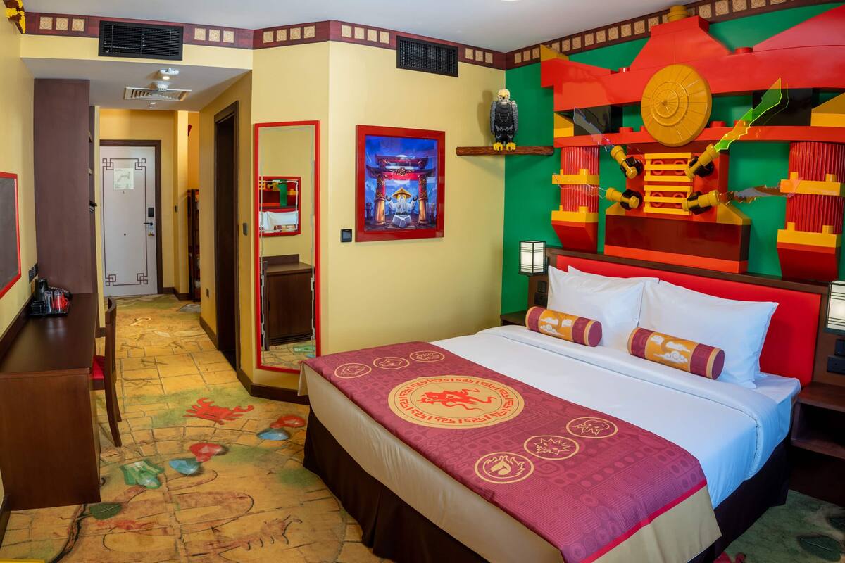 Una habitación de hotel con una cama, un escritorio y una pared decorada con obras de arte coloridas.