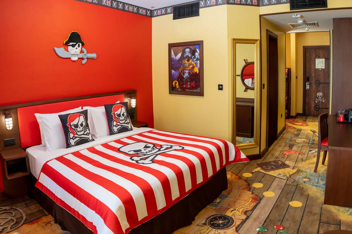 Una habitación con una cama, con un edredón de temática pirata, una almohada con calavera y tibias cruzadas, y un póster pirata enmarcado en la pared.