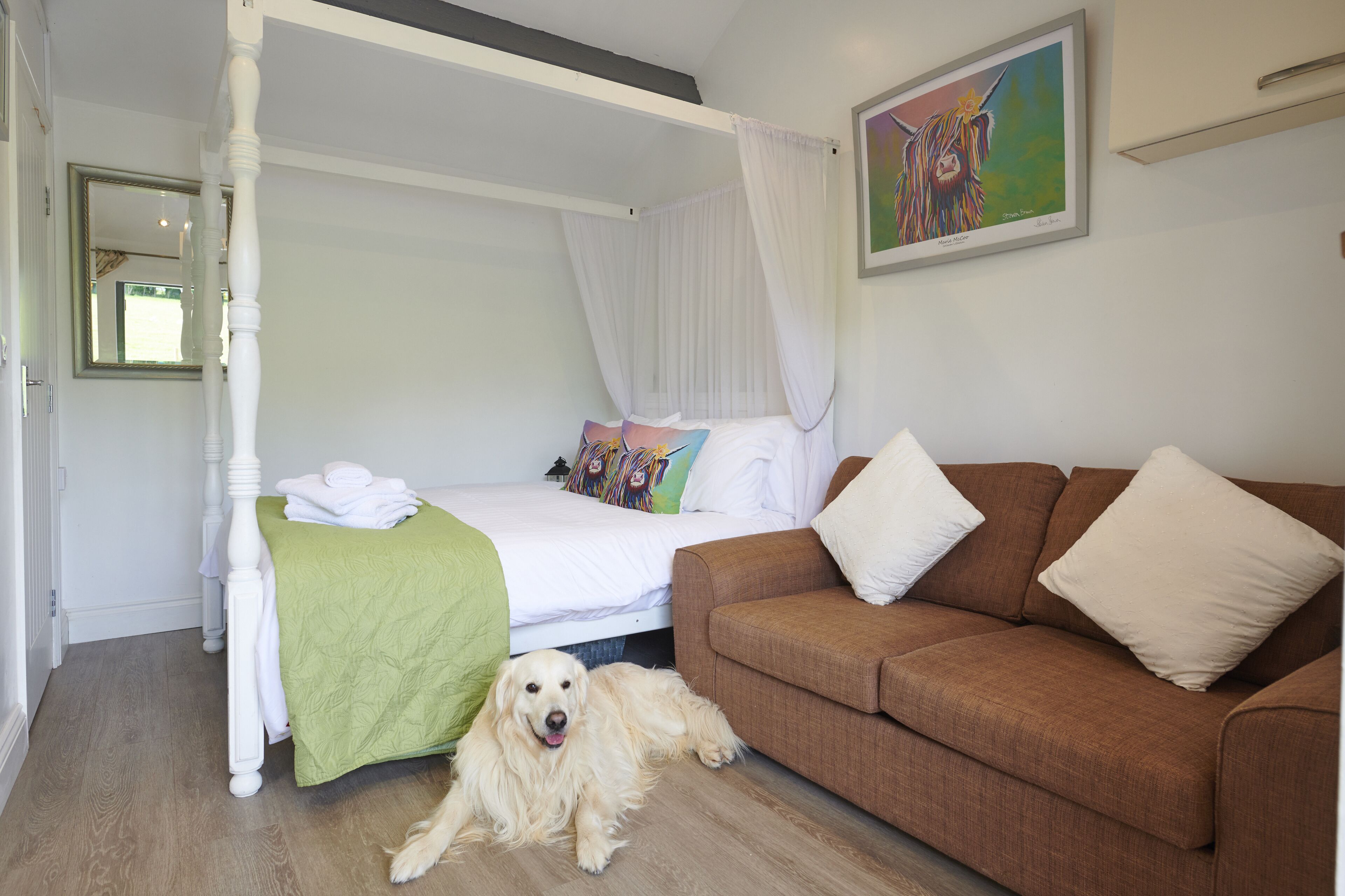 A bedroom with a four-poster bed, a brown sofa, and a dog lying on the floor.
