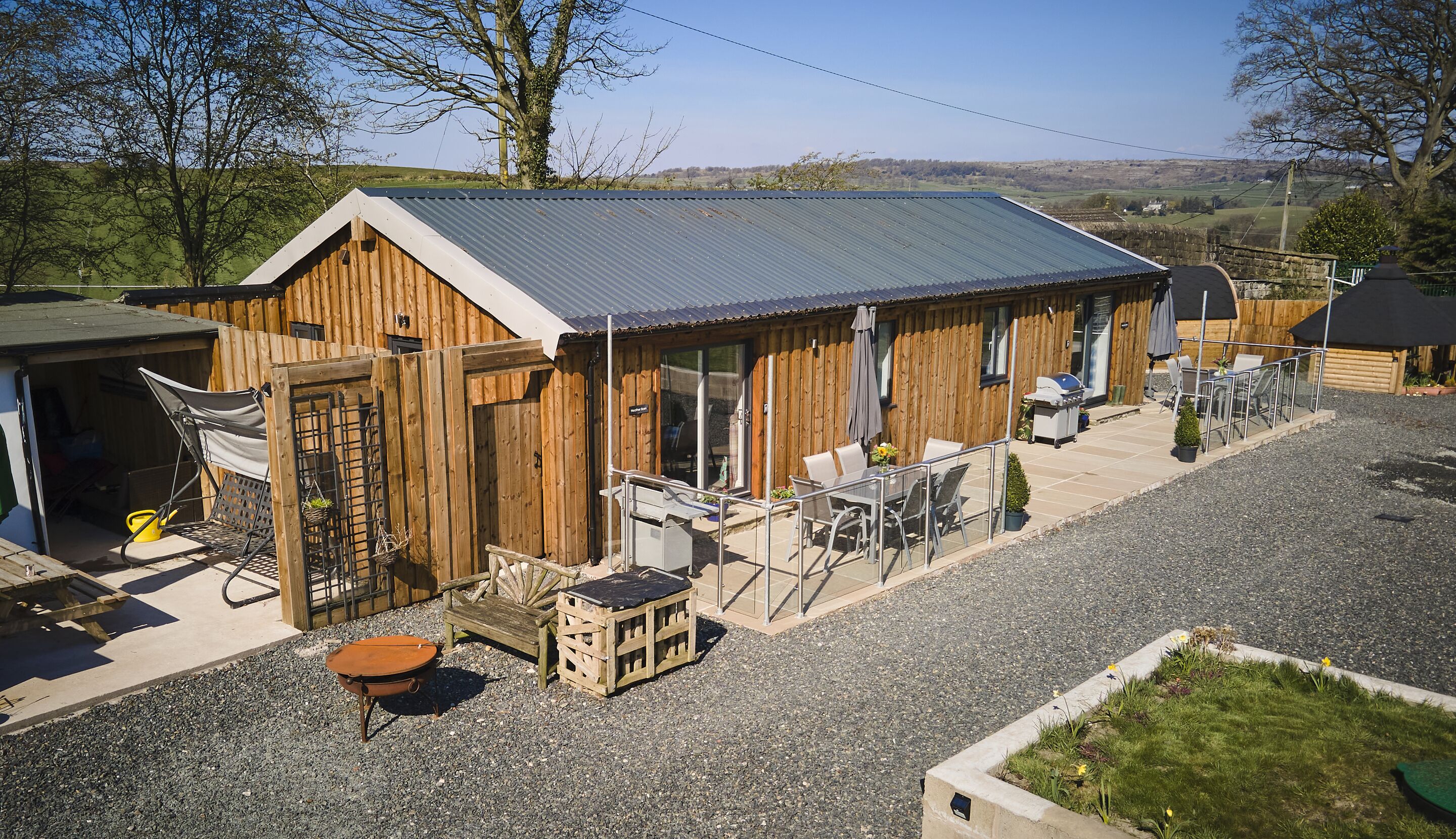 A wooden cabin with a metal roof, outdoor seating, and a gravel patio.