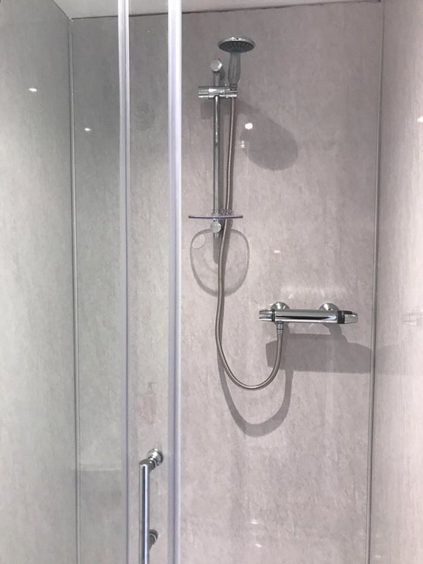 Une cabine de douche fermée par des parois en verre, équipée d’un pommeau de douche à main et d’un robinet à main.