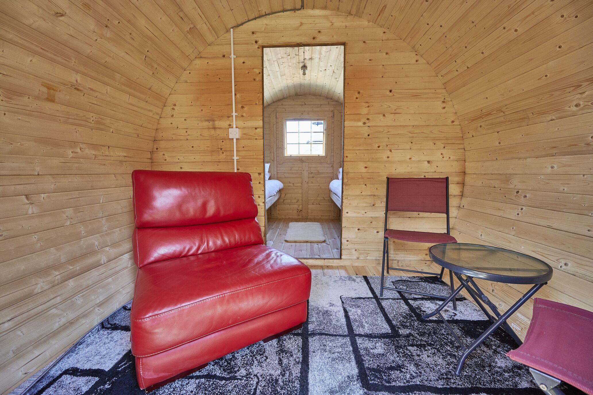 A cozy cabin with a red leather couch, a small round table, and a chair.