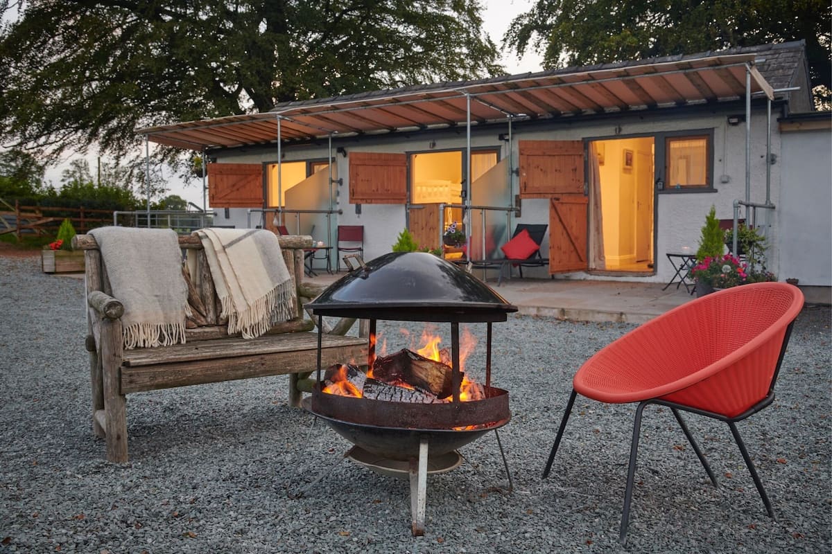 A cozy outdoor seating area with a fire pit, a red chair, and a wooden bench with a blanket.