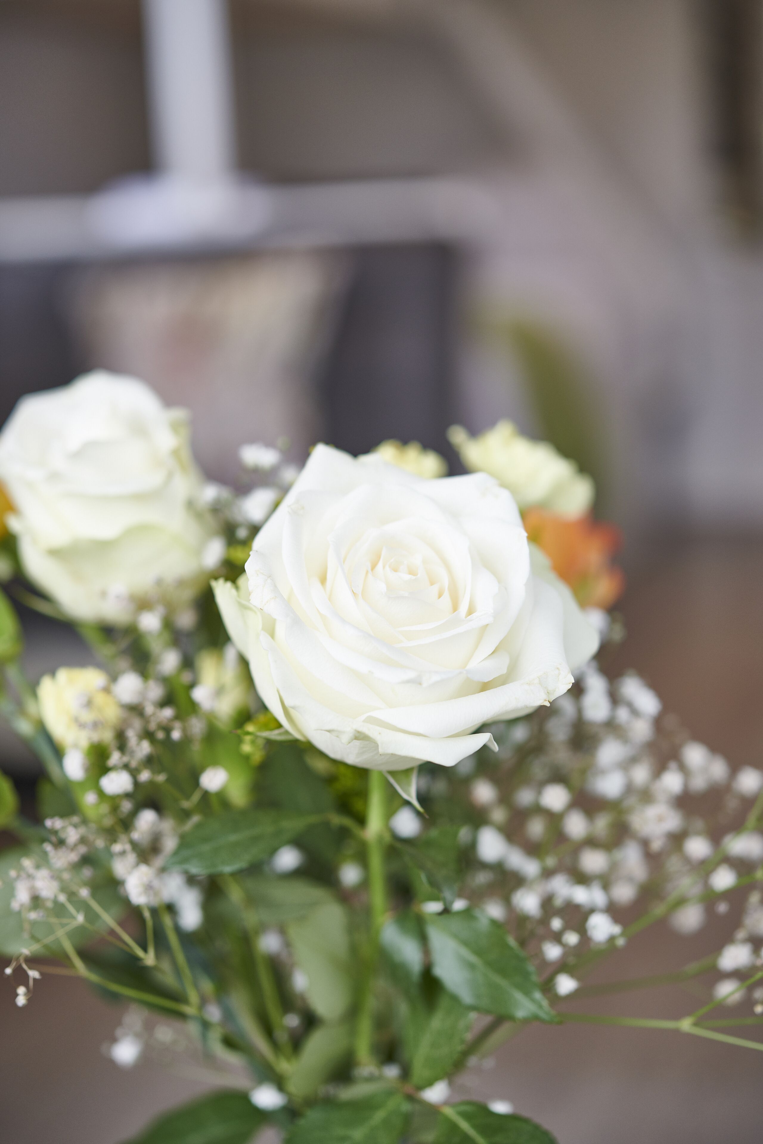 A bouquet of white roses with green leaves and small white flowers, placed in a clear glass vase.